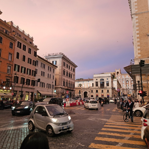 A busy city square at dusk under a pink sky