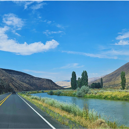 A river winding beside a highway through dry hills under a blue sky